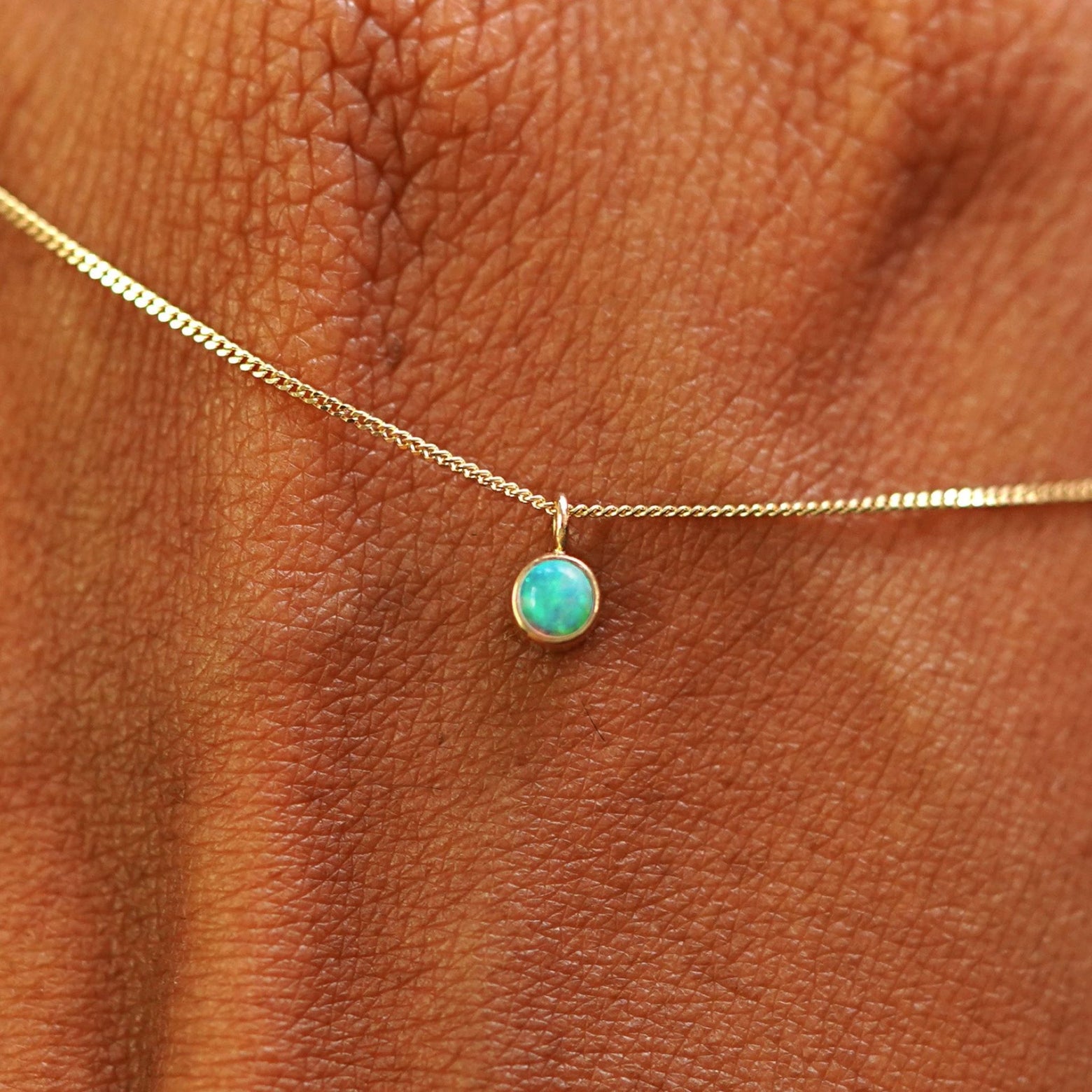 Close up view of a 14k yellow gold Opal Necklace draped across the back of a model's hand
