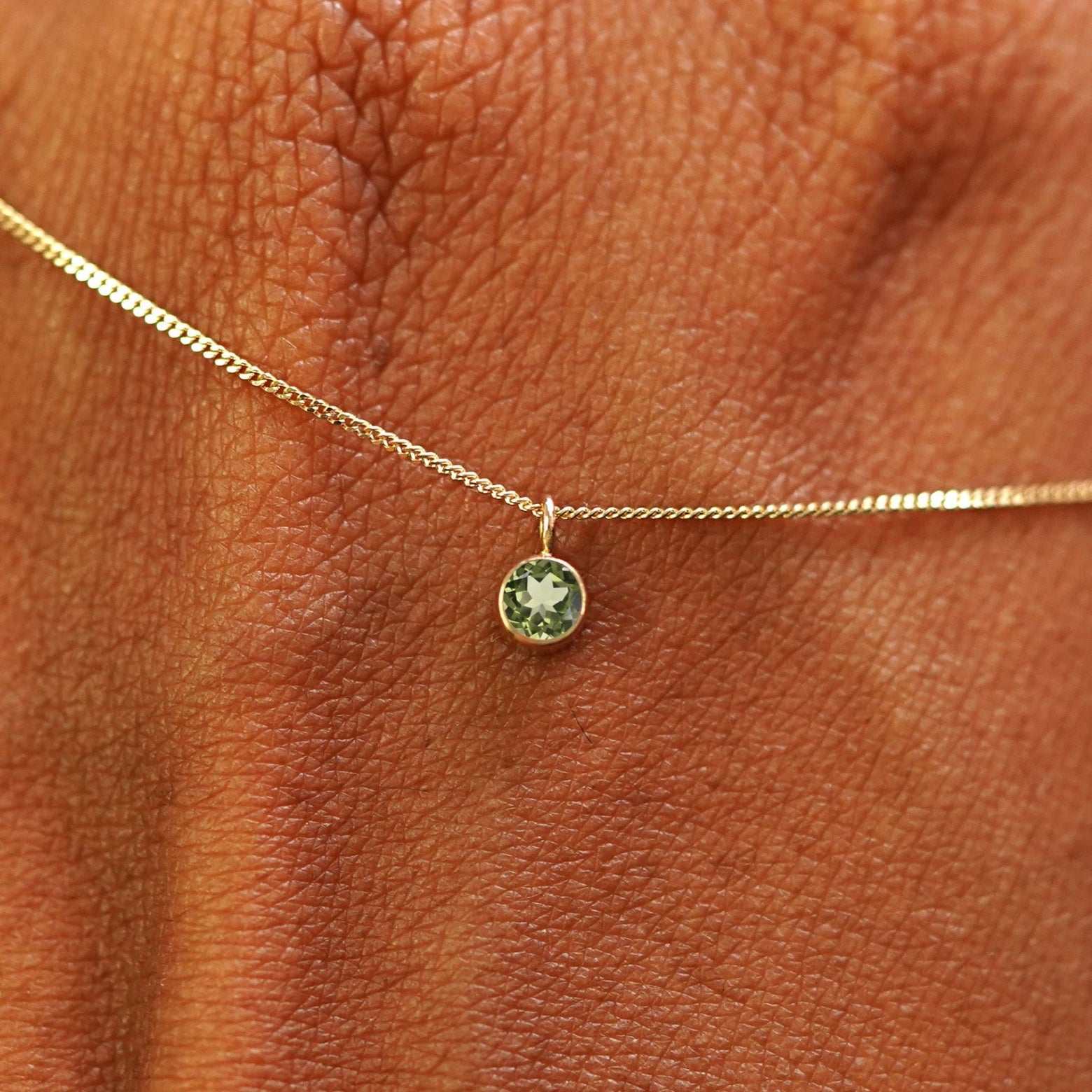 Close up view of a 14k yellow gold Peridot Necklace draped across the back of a model's hand