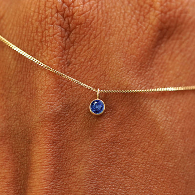 Close up view of a 14k yellow gold Sapphire Necklace draped across the back of a model's hand