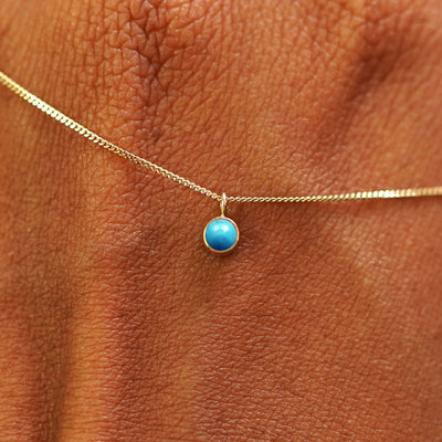 Close up view of a 14k yellow gold Turquoise Necklace draped across the back of a model's hand