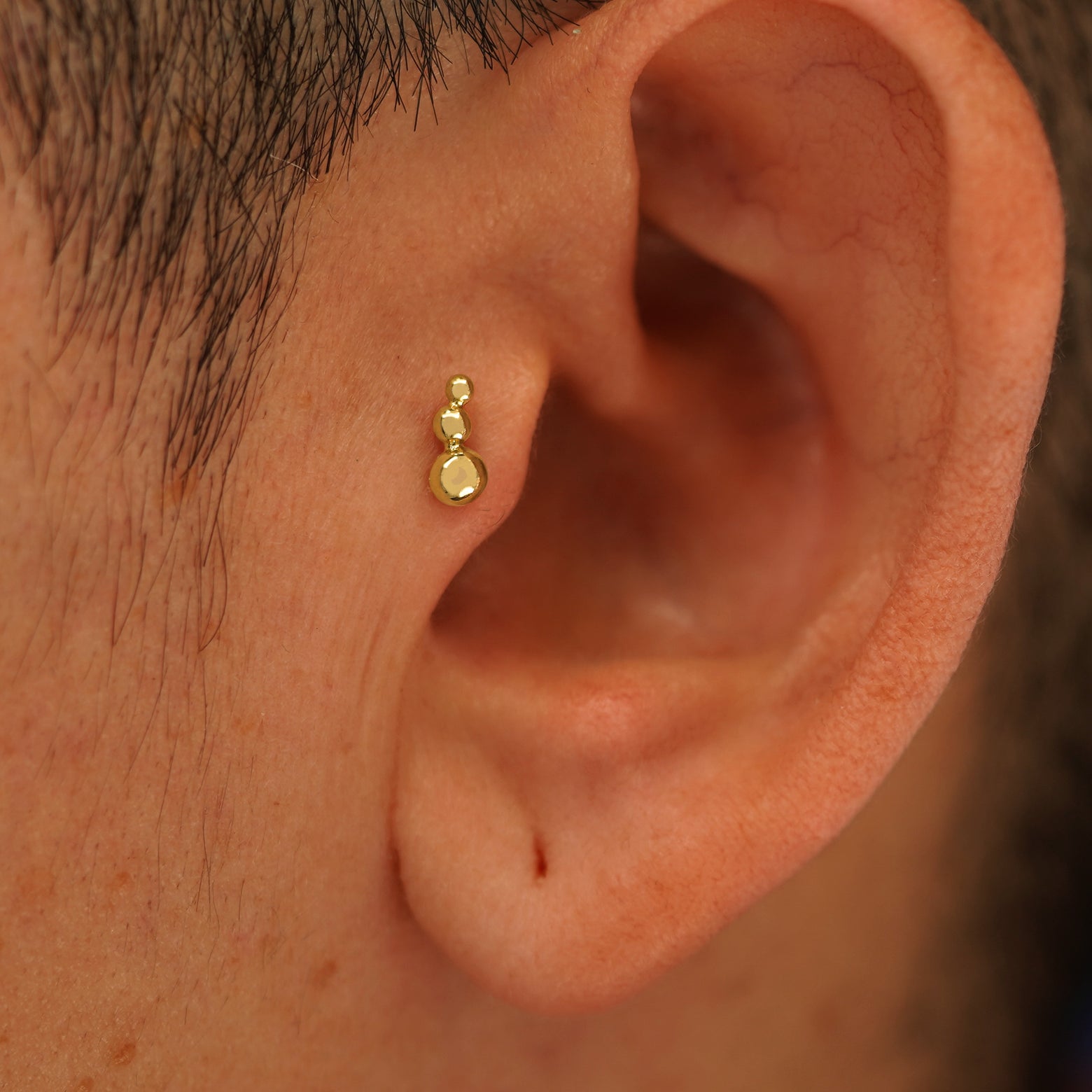 Close up view of a model's ear wearing a 14k yellow gold Graduated Ball Flatback as a tragus piercing