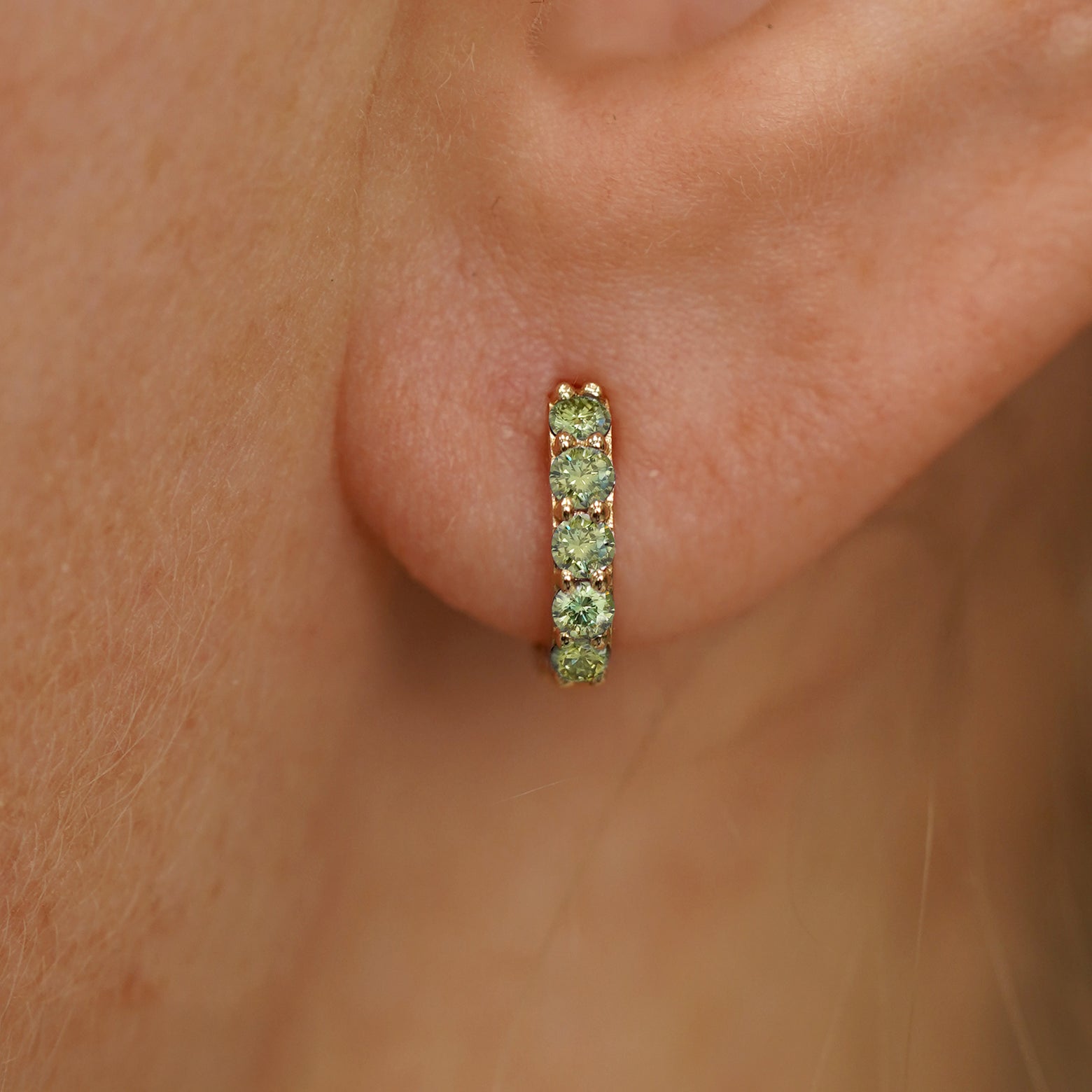 Close up view of a model's ear wearing a yellow gold Mini Light Green Lab Diamond Huggie Hoop