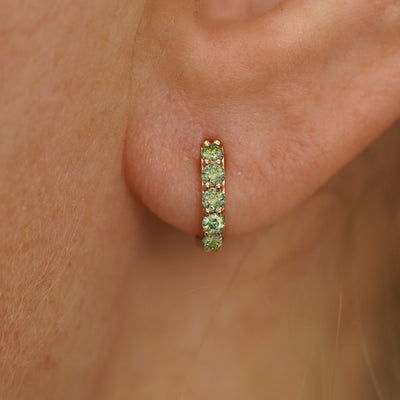 Close up view of a model's ear wearing a yellow gold Mini Light Green Lab Diamond Huggie Hoop
