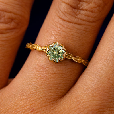 A solid 14k yellow gold Green Moissanite Leaf Ring on a model's finger
