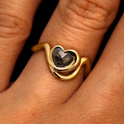 A model's hand wearing a 14k yellow gold Heart Salt and Pepper Diamond Infinite Wave Ring
