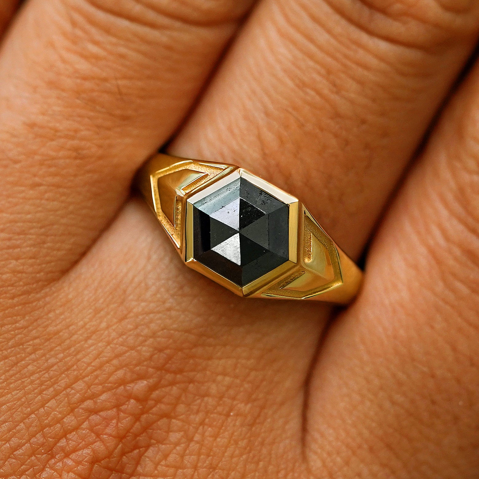 Close up view of a model's fingers wearing a 14k yellow gold hexagon black diamond engraved transformation ring