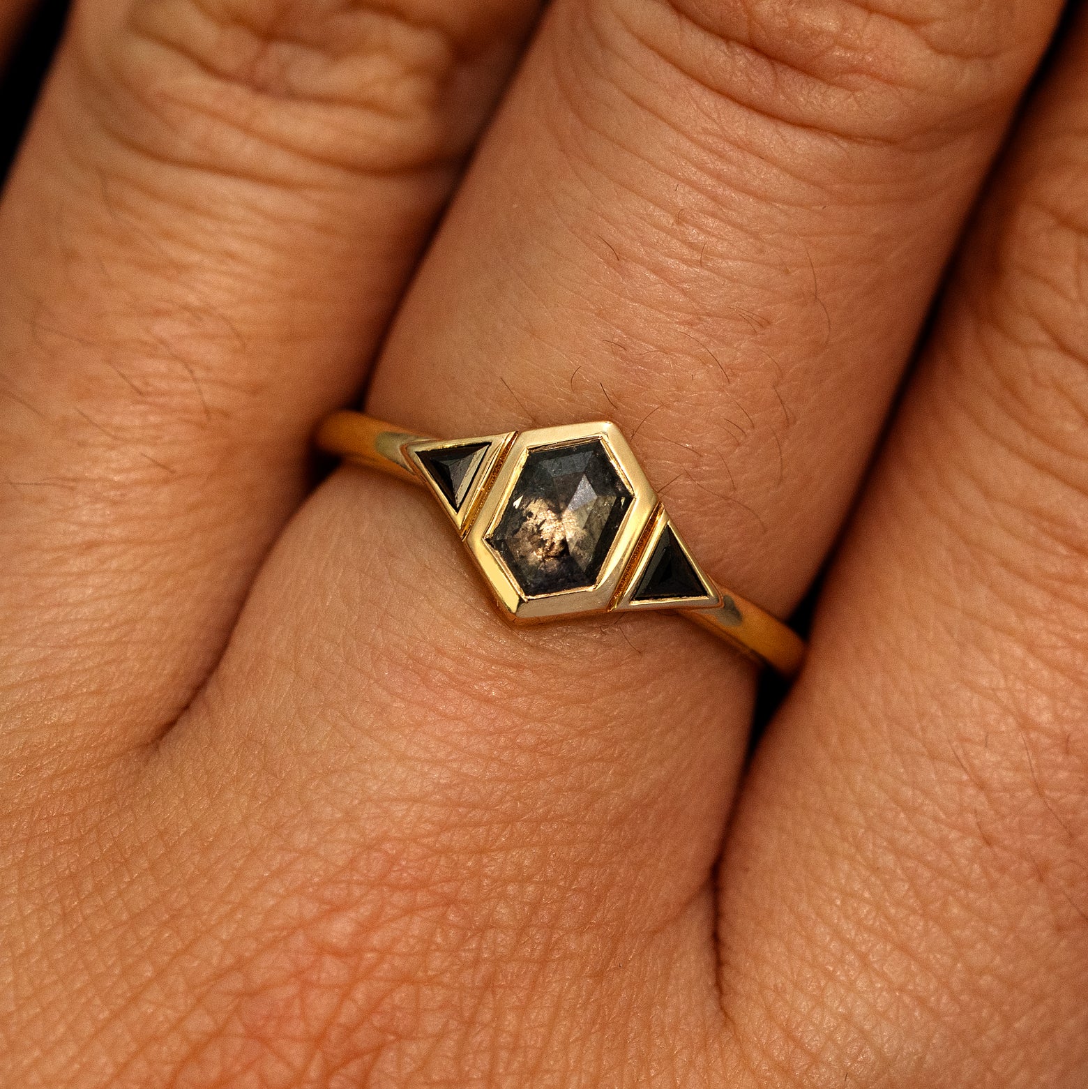 A model's hand wearing a 14k yellow gold Hexagon Salt and Pepper and Triangle Black Diamond Three Stone Ring