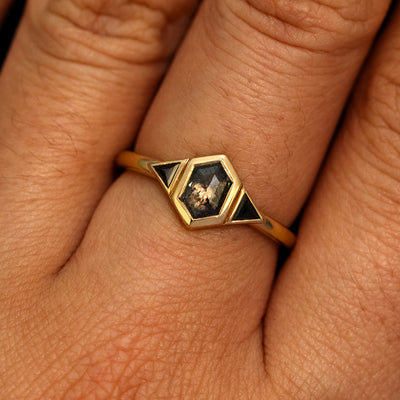 A model's hand wearing a 14k yellow gold Hexagon Salt and Pepper and Triangle Black Diamond Three Stone Ring
