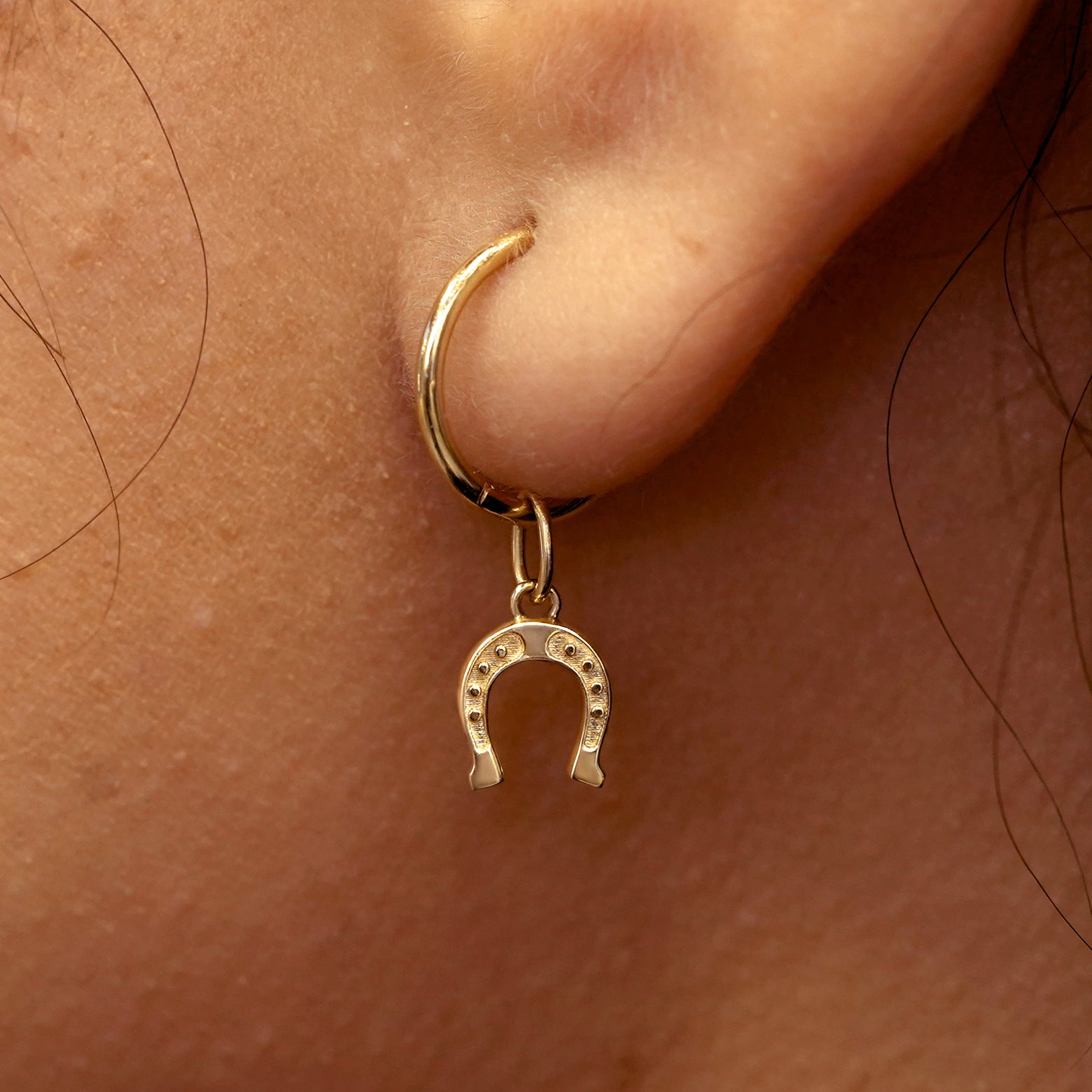 Close up view of a model's ear wearing a yellow gold Horseshoe Charm on a Small Seamless Huggie Hoop