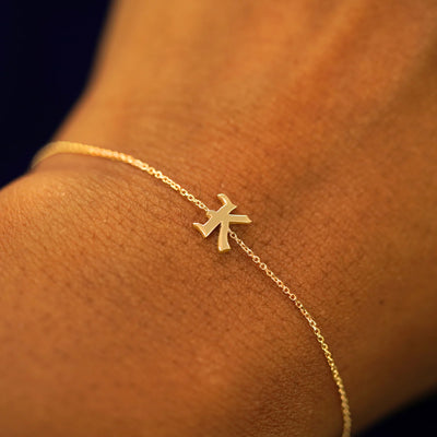 A model's wrist wearing a 14k solid yellow gold Initial Bracelet in the letter K