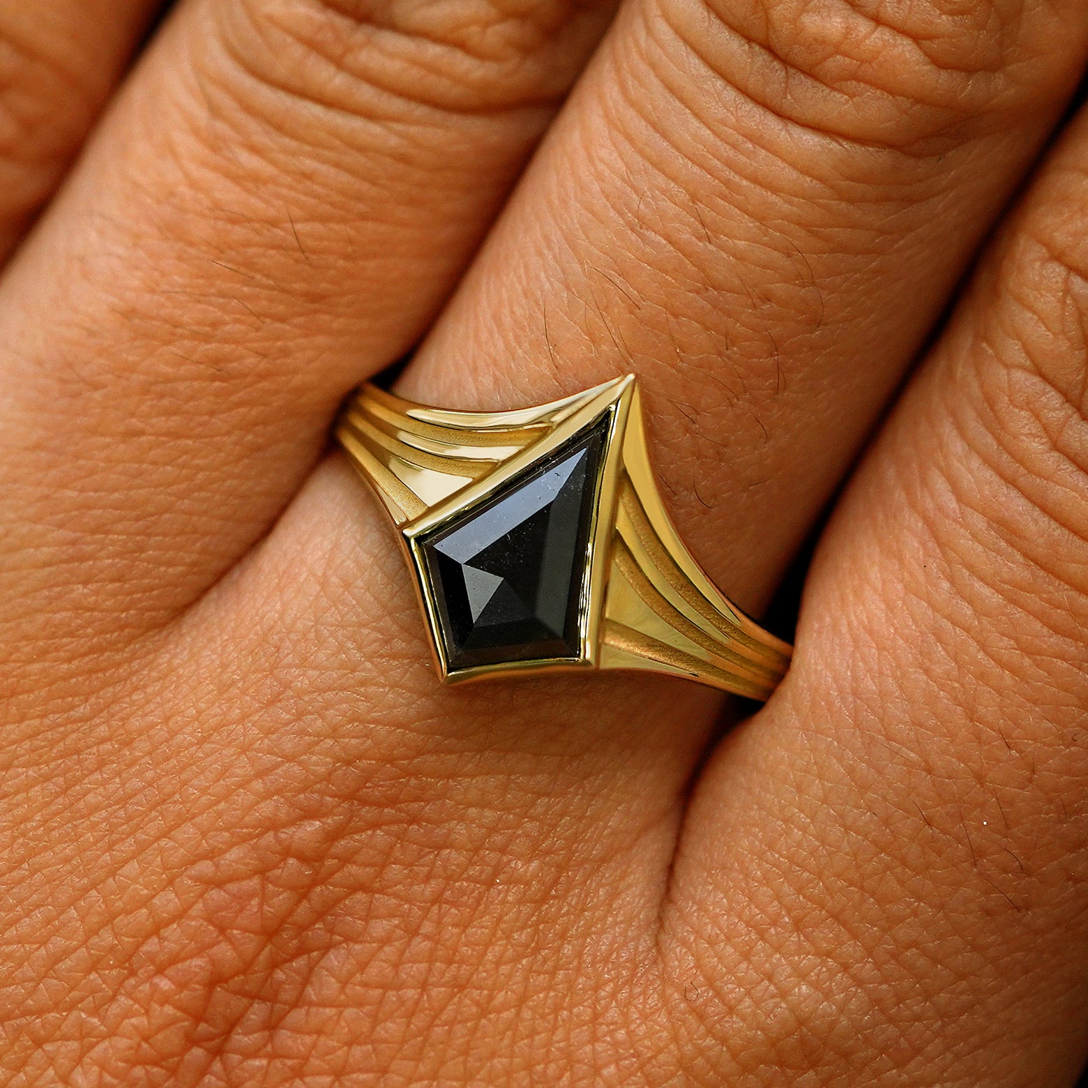Close up view of a model's fingers wearing a 14k yellow gold kite black diamond engraved journey ring