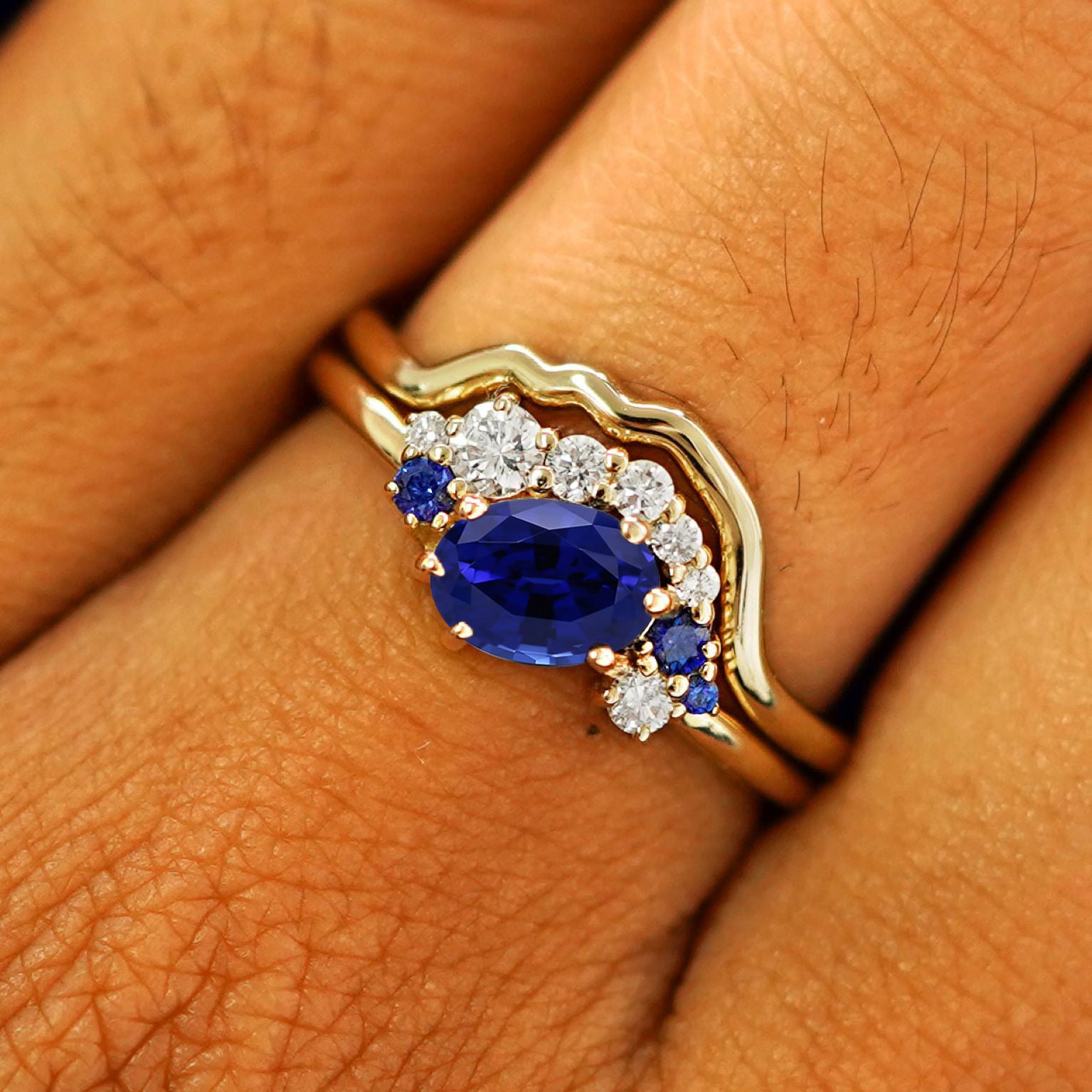 Close up view of a model's fingers wearing a 14k yellow gold Lab Sapphire and Diamond Cluster Ring Set