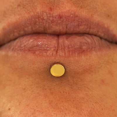 Close up view of a model's lips wearing a 14k yellow gold Large Circle Flatback in a labret piercing