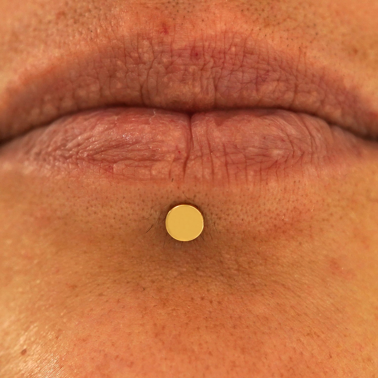 Close up view of a model's lips wearing a 14k yellow gold Medium Circle Flatback in a labret piercing