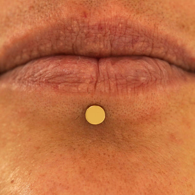 Close up view of a model's lips wearing a 14k yellow gold Medium Circle Flatback in a labret piercing