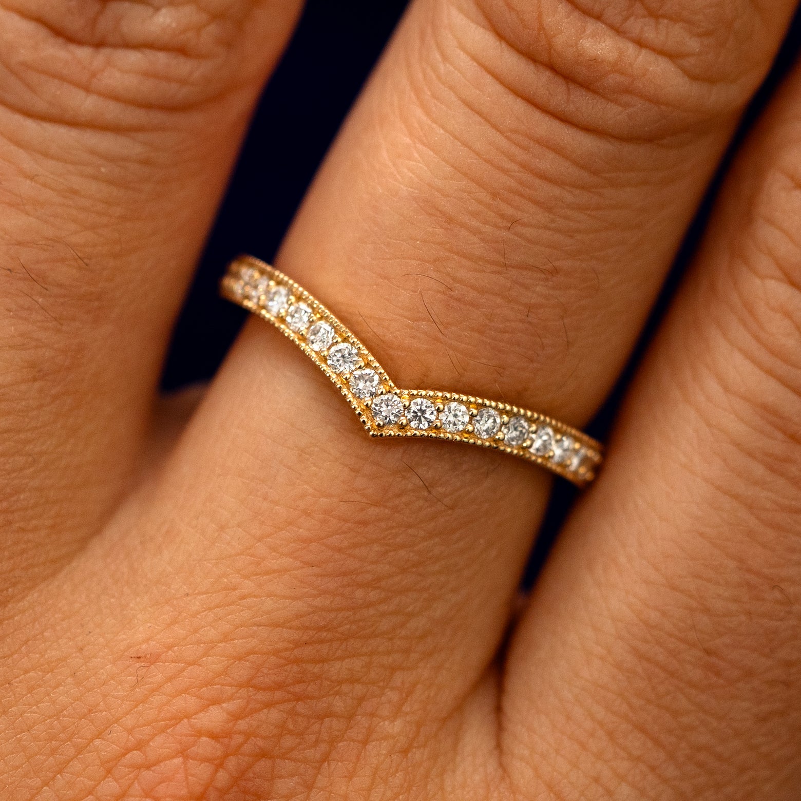 Close up view of a model's fingers wearing a 14k yellow gold Milgrain Pave Diamond Chevron Band