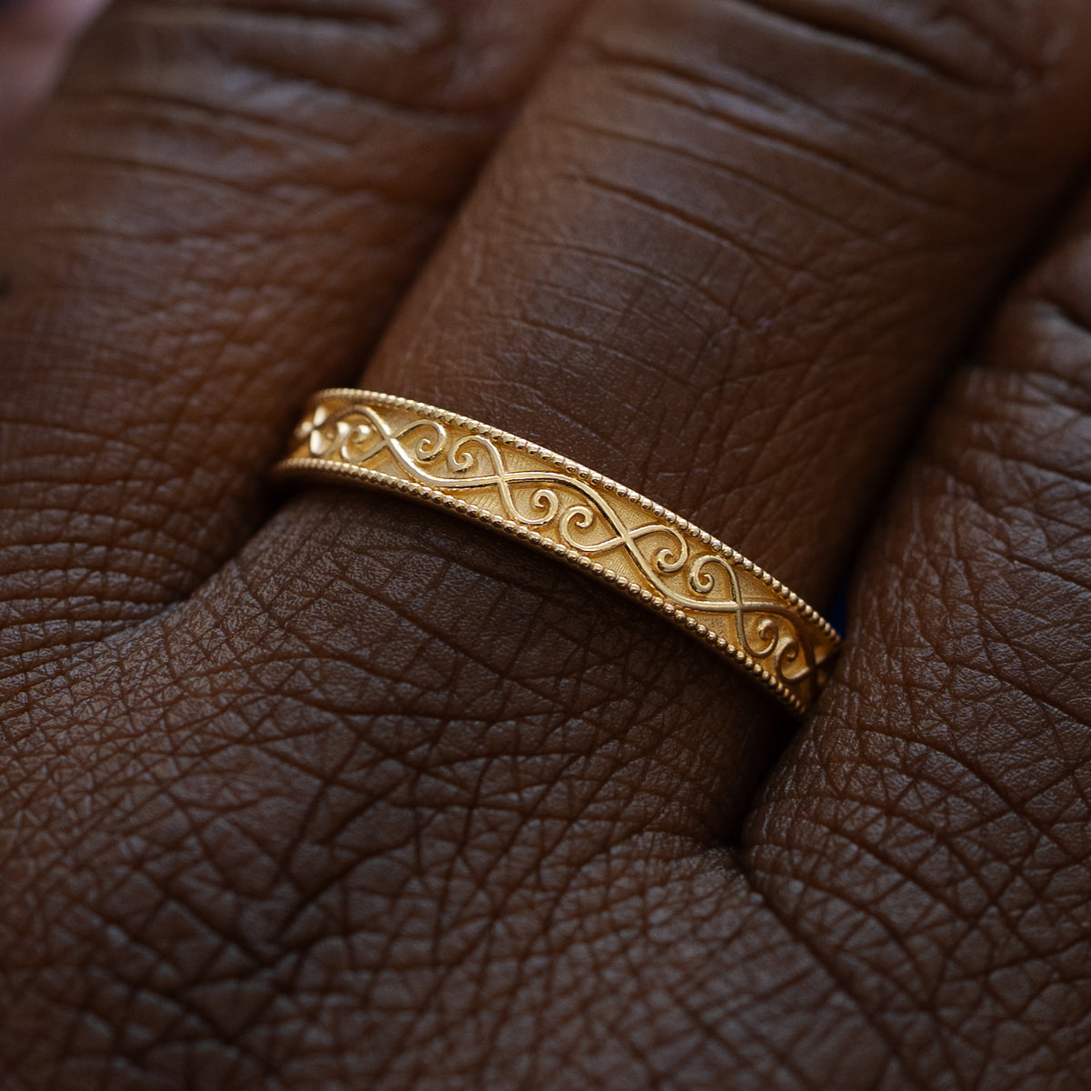 Close up view of a model wearing a solid 14k yellow gold milgrain scroll band