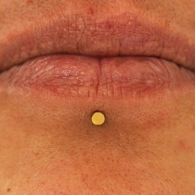 Close up view of a model's lips wearing a 14k yellow gold Mini Circle Flatback in a labret piercing
