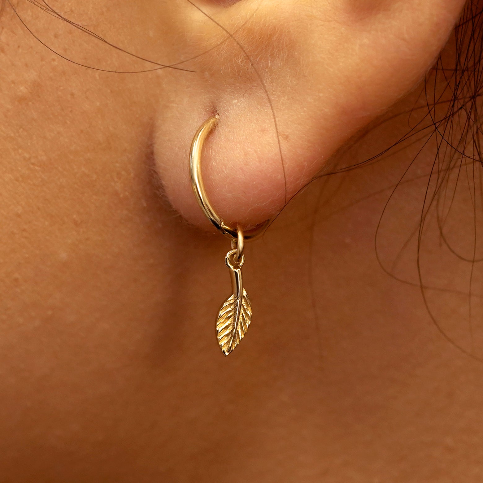 Close up view of a model's ear wearing a yellow gold Leaf Charm on a Small Seamless Huggie Hoop