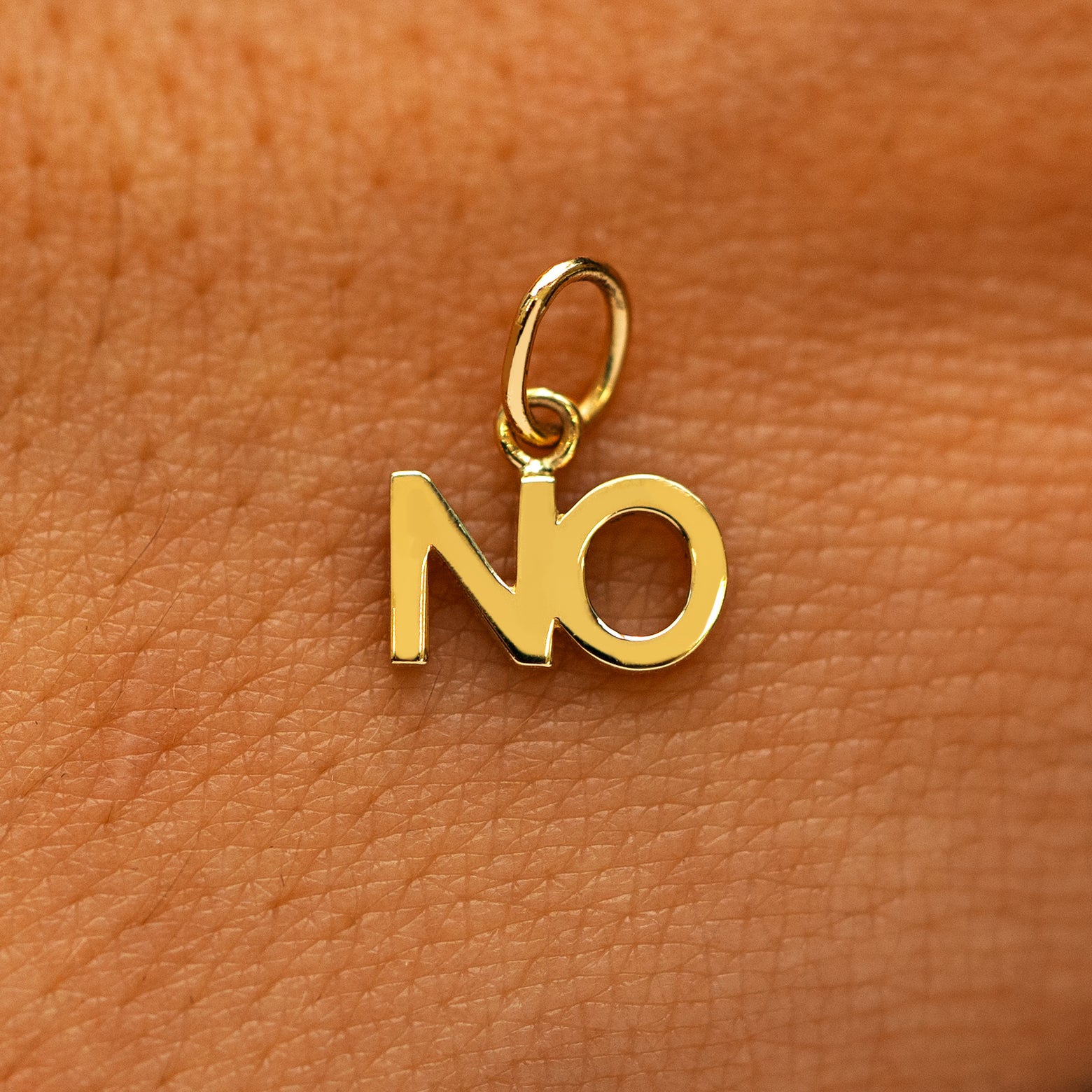 A solid 14k yellow gold No Charm on the back of a models hand
