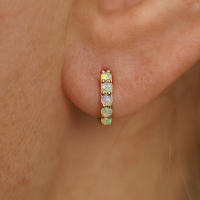 Close up view of a model's ear wearing a yellow gold Mini Opal Huggie Hoop