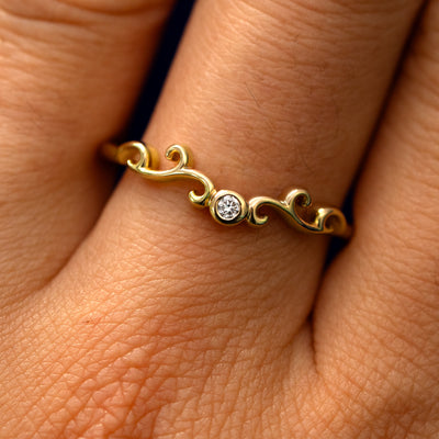 Close up view of a model's fingers wearing a 14k yellow gold Open Filigree Chevron Diamond Band