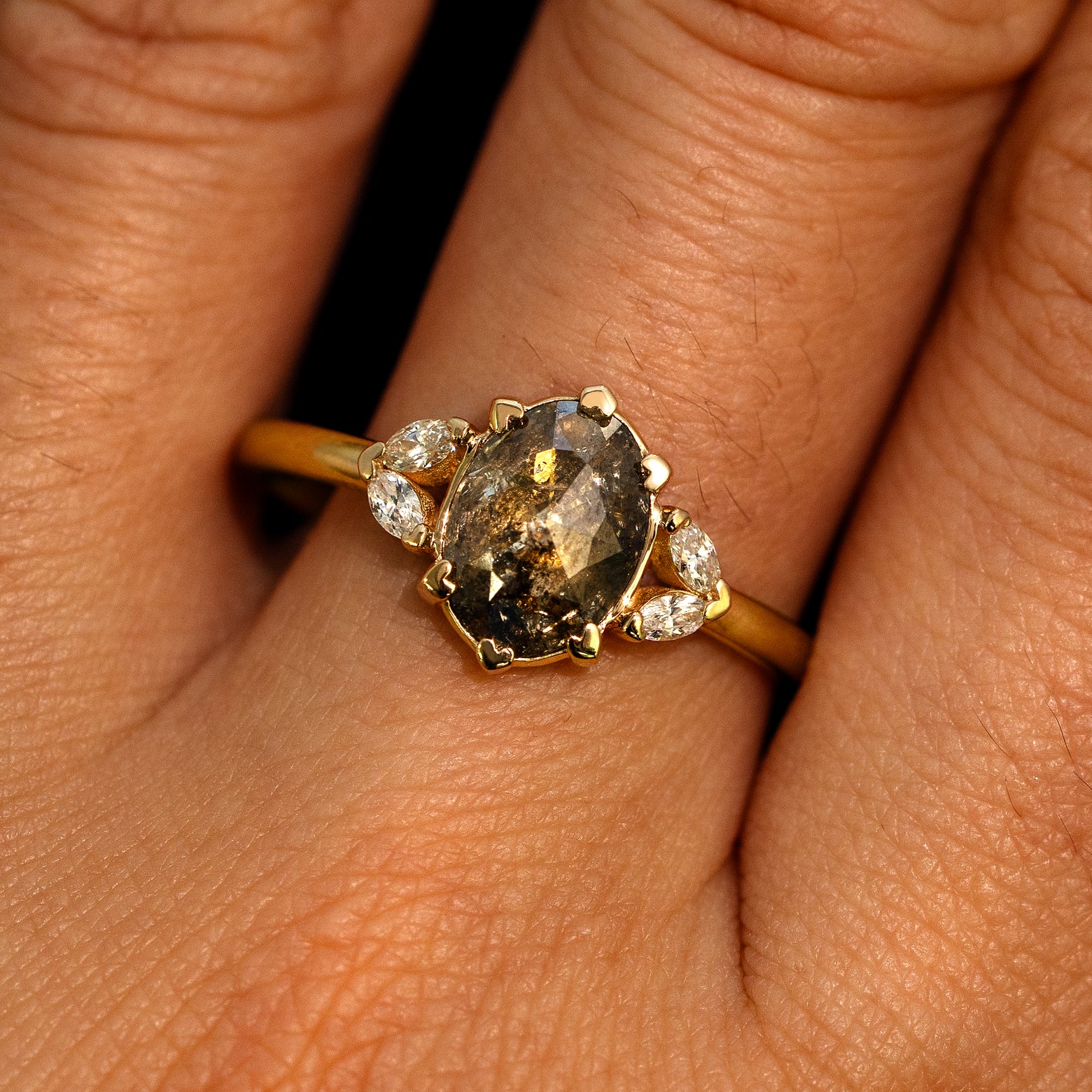 A model's hand wearing a 14k yellow gold Oval Salt and Pepper Diamond Heart Prong Ring
