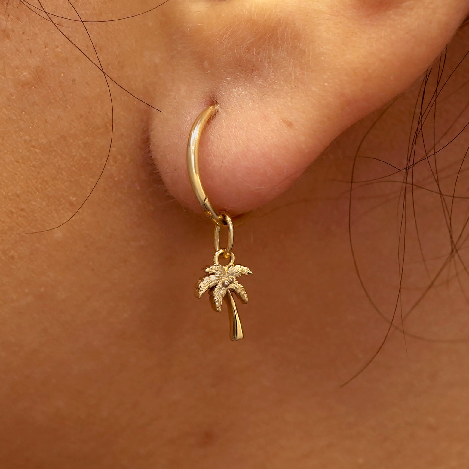 Close up view of a model's ear wearing a yellow gold Palm Tree Charm on a Small Seamless Huggie Hoop