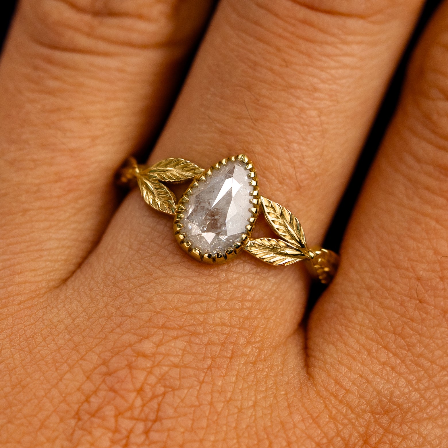 Close up view of a model's fingers wearing a 14k yellow gold Pear Salt and Pepper Diamond Leaves Ring