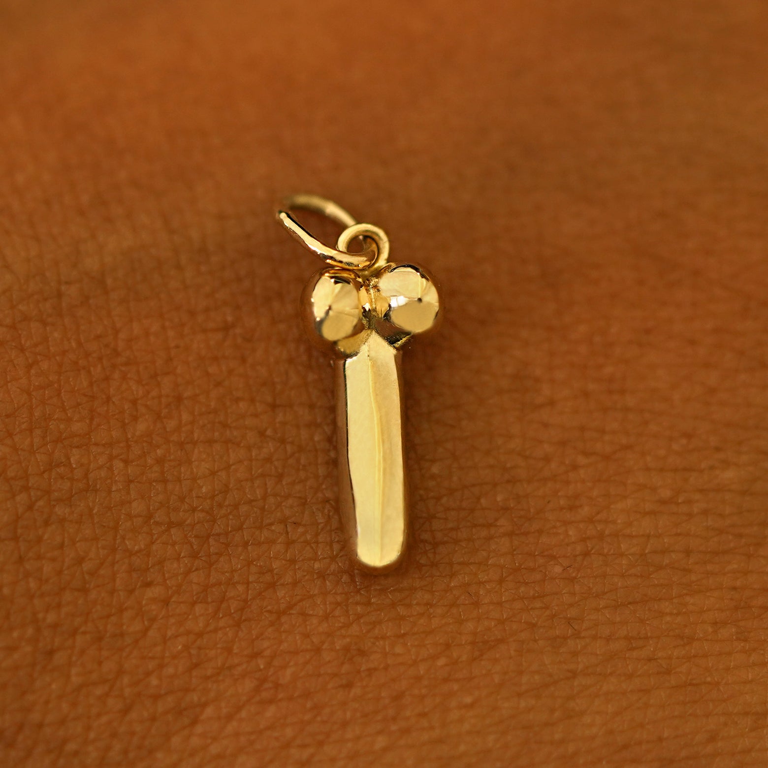 A 14k yellow gold penis charm on the back of a models hand
