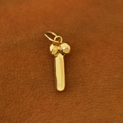 A 14k yellow gold penis charm on the back of a models hand