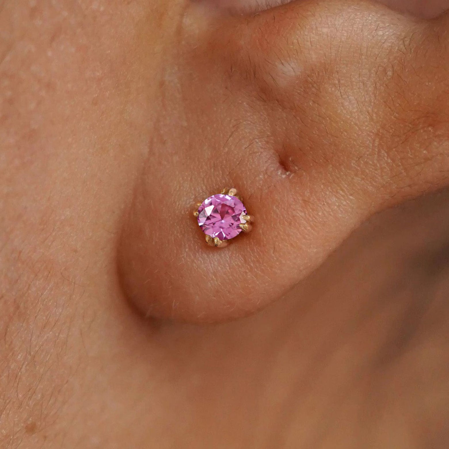Close up view of a model's ear wearing a 14k yellow gold Pink Sapphire Earring