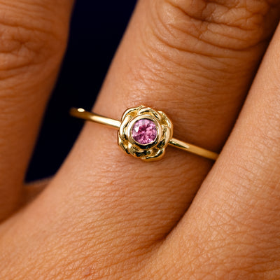 A solid 14k yellow gold Pink Sapphire Gemstone Flower Ring on a model's finger