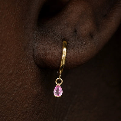 Close up view of a model's ear wearing a yellow gold Pink Sapphire Dangle Huggie Hoop