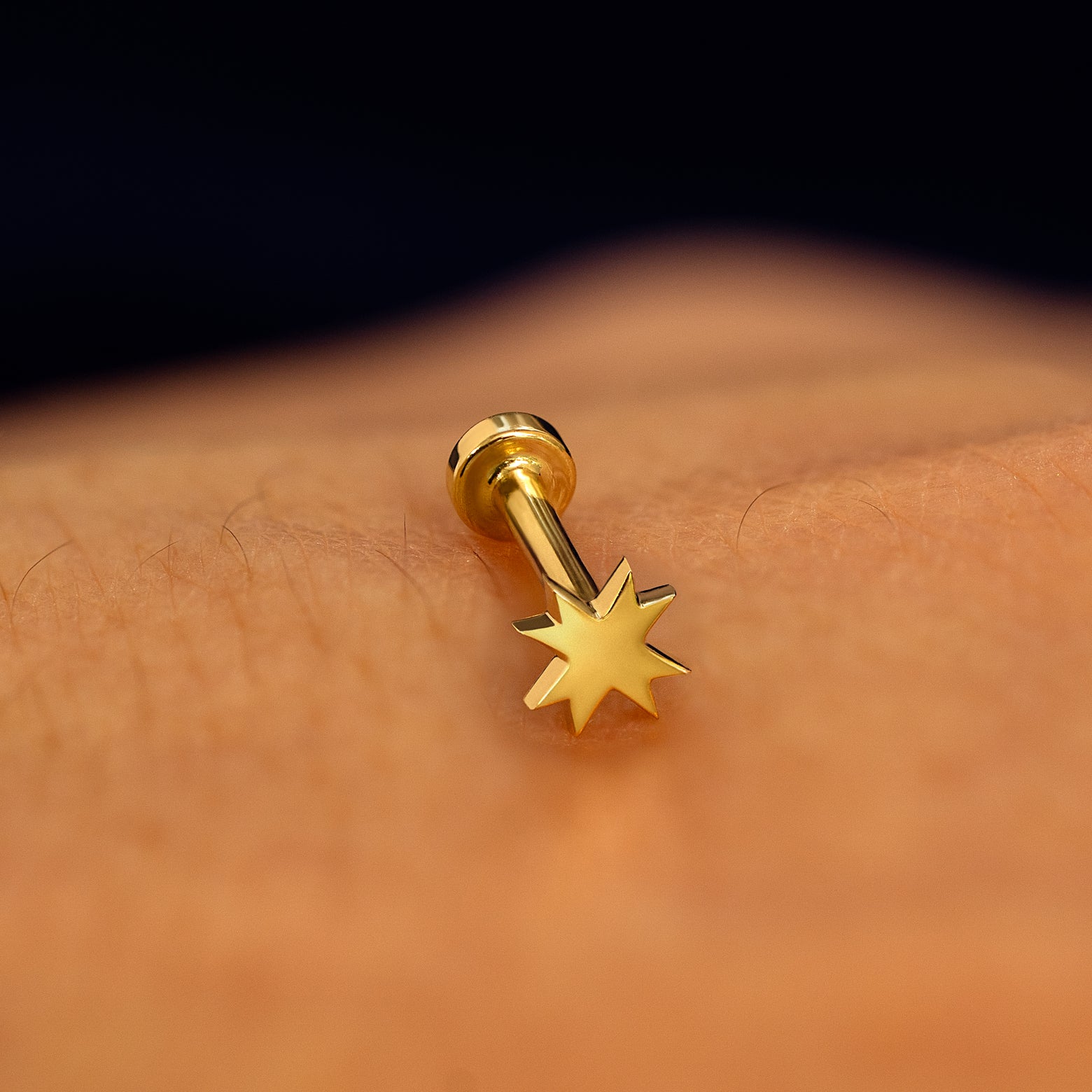A yellow gold 8 pointed star flatback piercing with yellow gold backing on a models hand