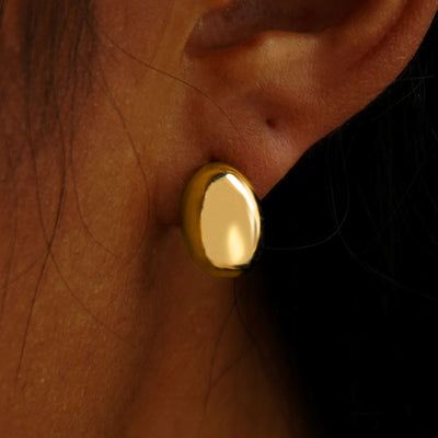 Close up view of a model's ear wearing a 14k yellow gold Oval Puffy Earring