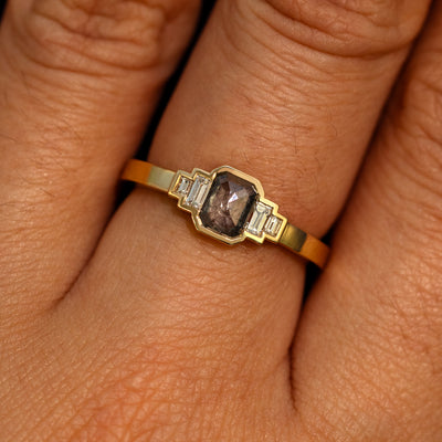 Close up view of a model's hand wearing a 14k yellow gold Emerald Cut Salt and Pepper and Clear Baguette Diamond Ring