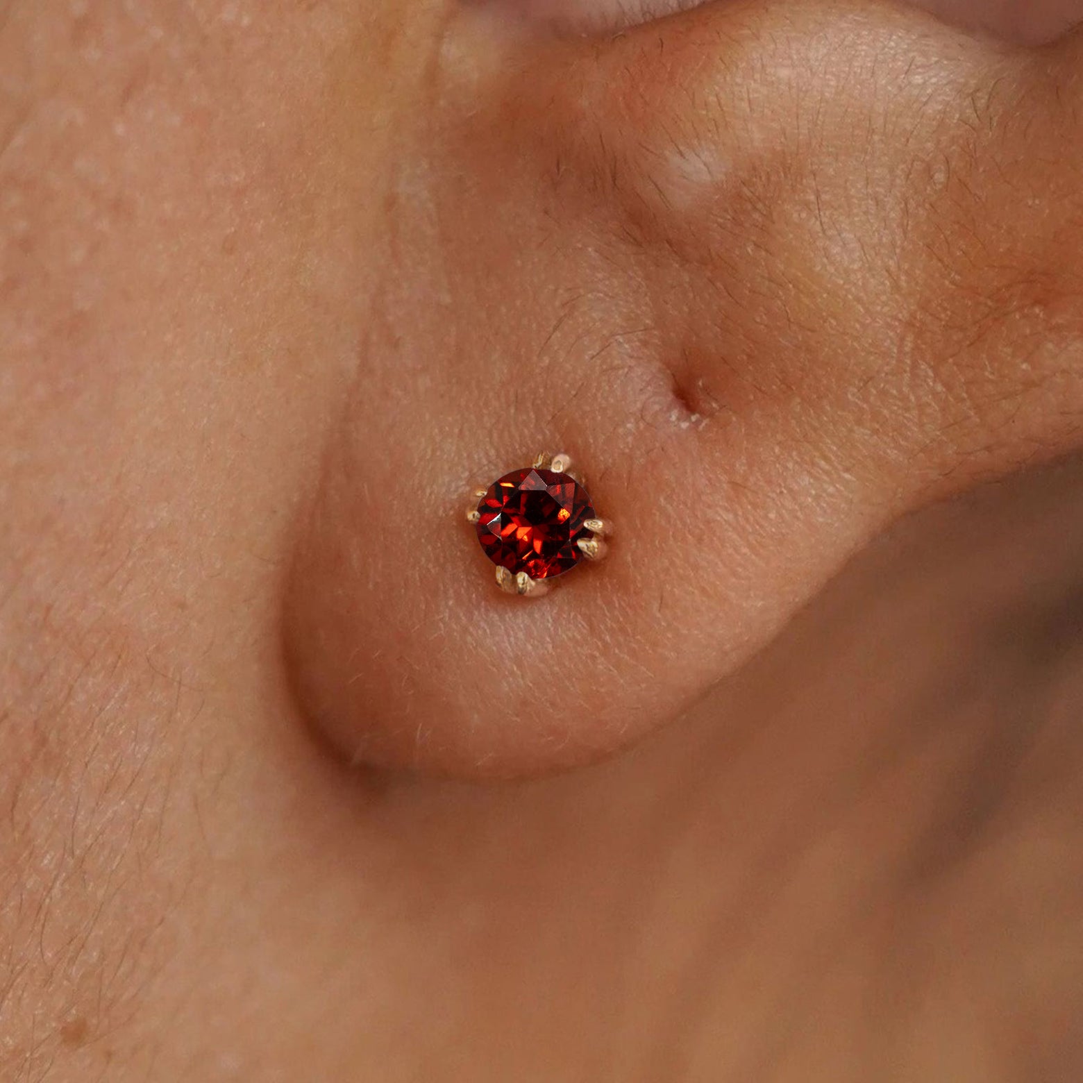 Close up view of a model's ear wearing a 14k yellow gold Garnet Earring