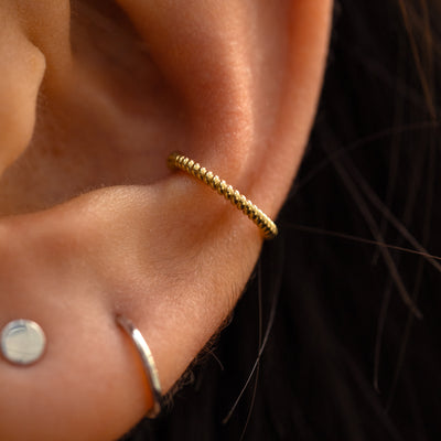 A close up of someone's ear with a 14k yellow gold rope cuff attached on their  outer ear.