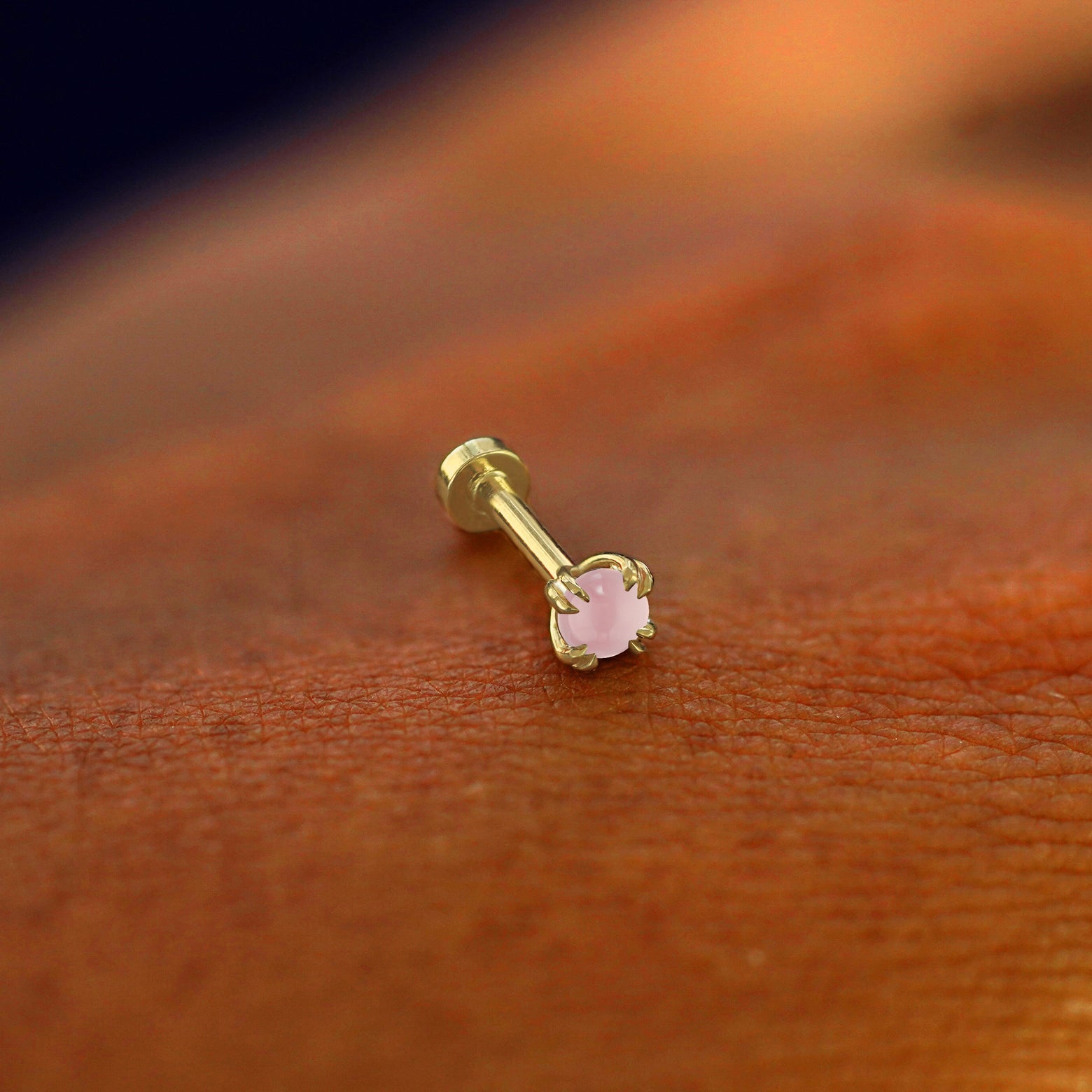 A solid 14k yellow gold Rose Quartz Flatback Piercing resting on the back of a model's hand