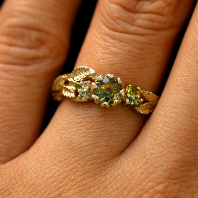Close up view of a model's fingers wearing a 14k gold Green Sapphire Leaves and Vines Ring