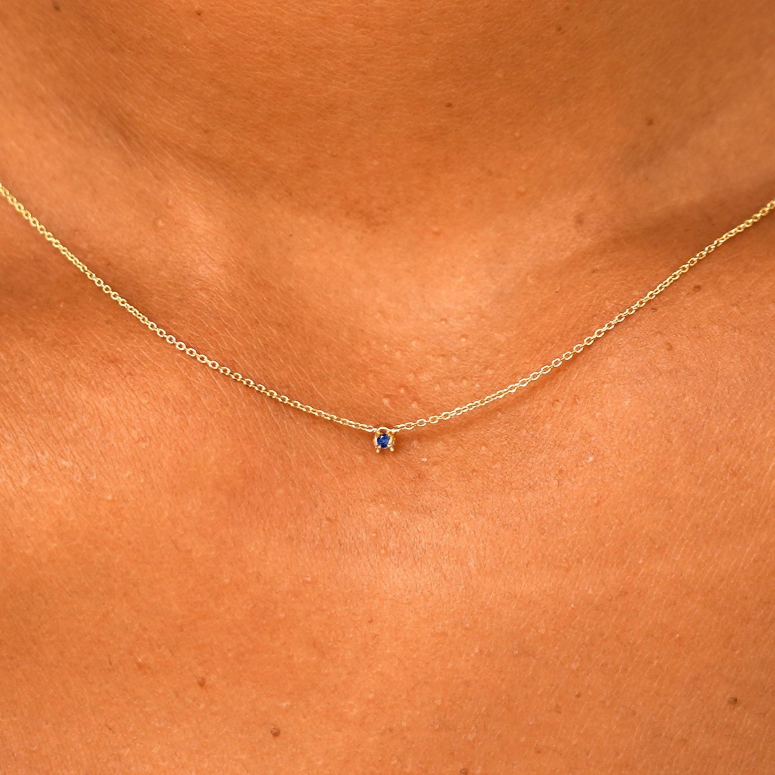 Close up view of a model's neck wearing a solid 14k yellow gold Gemstone Cable Necklace in sapphire