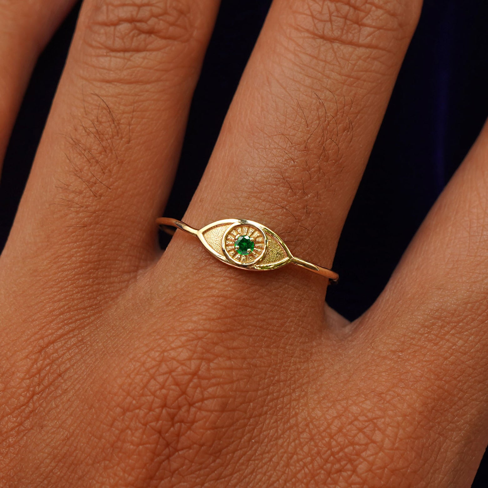Close up view of a model's hand wearing a yellow gold Evil Eye Ring in the Emerald gemstone option