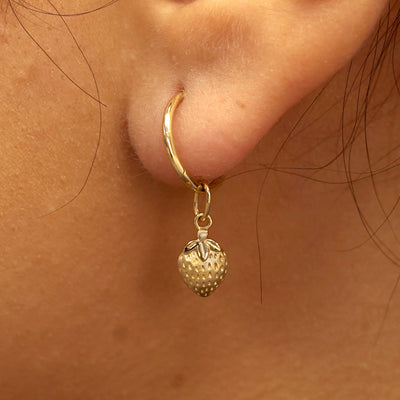 Close up view of a model's ear wearing a yellow gold Strawberry Charm on a Small Seamless Huggie Hoop