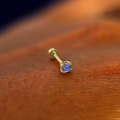 A solid 14k yellow gold Tanzanite Flatback Piercing resting on the back of a model's hand