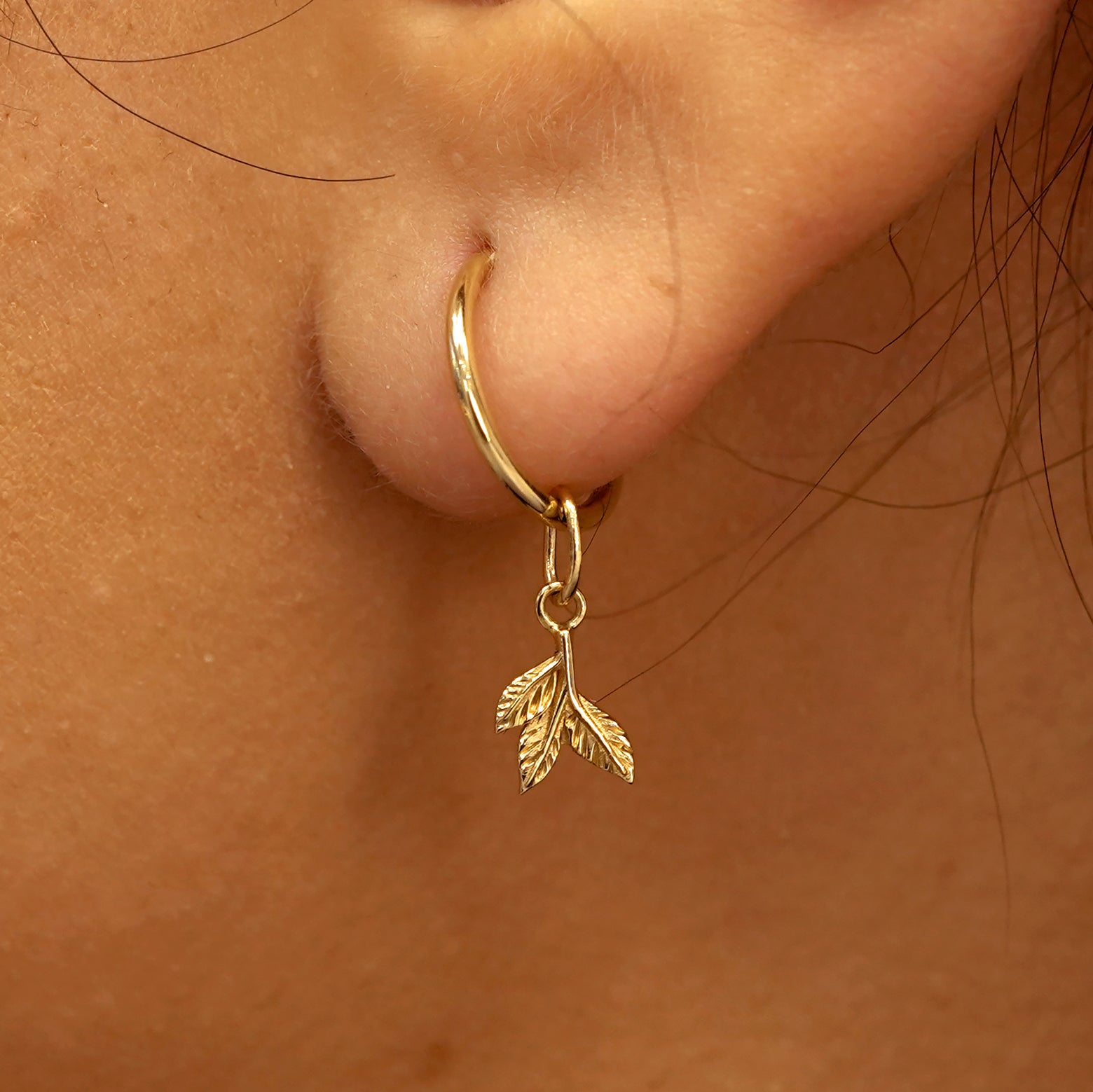 Close up view of a model's ear wearing a yellow gold 3 Leaves Charm on a Small Seamless Huggie Hoop