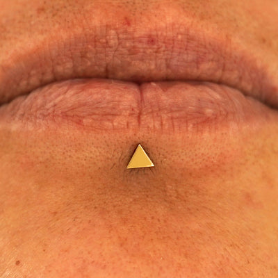 Close up view of a model's lips wearing a 14k yellow gold Triangle Flatback in a labret piercing
