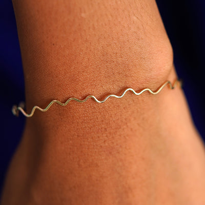 Close up view of a model's wrist wearing a yellow gold Wave Bangle Bracelet