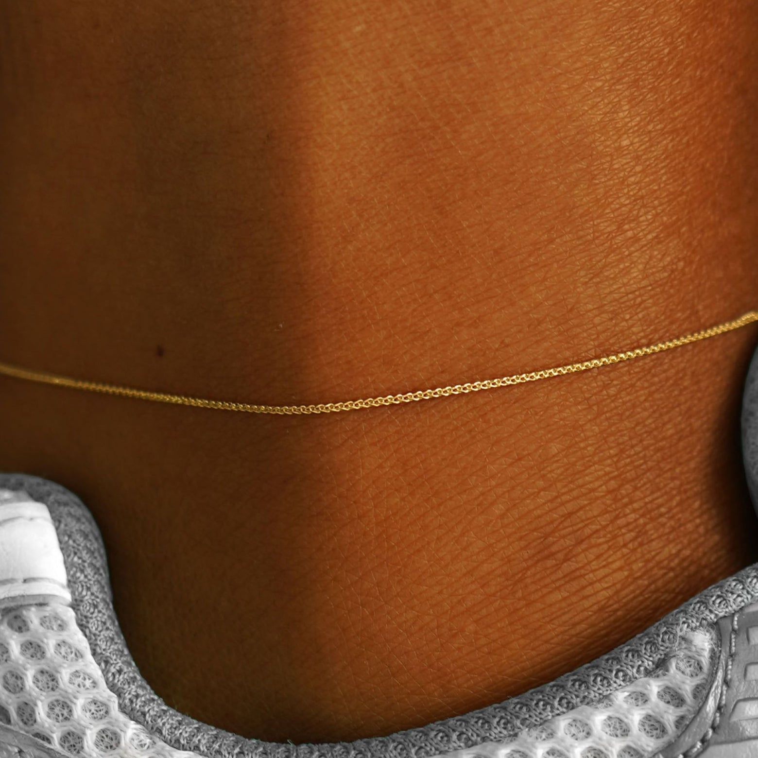 Close up view of a model's ankle wearing a solid 14k yellow gold Wheat Chain