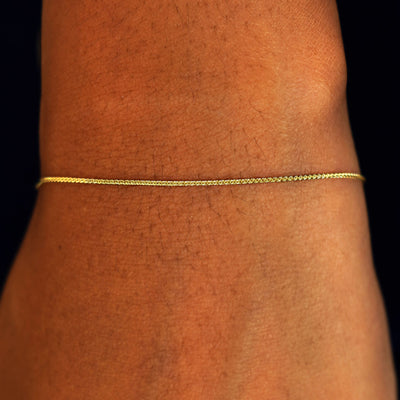 A model's wrist wearing a solid 14k yellow gold Wheat Chain